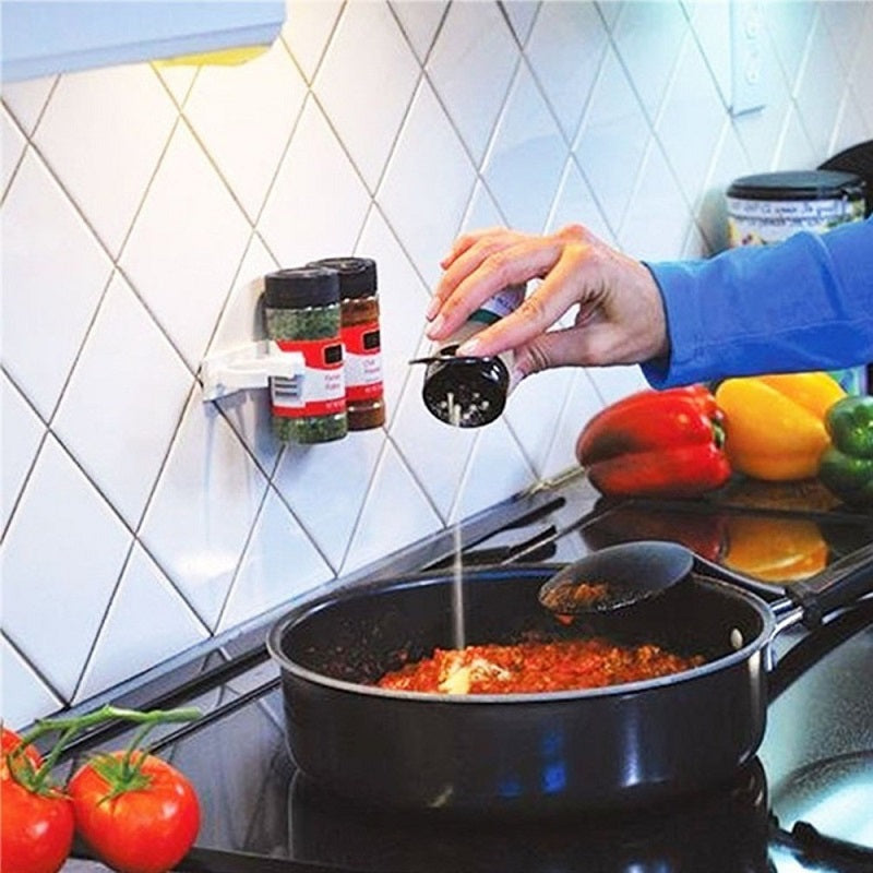 Adhesive spice rack mounted on a kitchen wall holding two spice jars near a stovetop while cooking