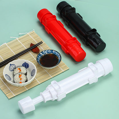 Red, black, and blue sushi making tools next to a bowl of finished sushi rolls and soy sauce