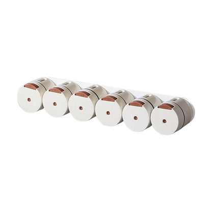 Six white magnetic seasoning canisters with brown lids arranged in a row on a white background