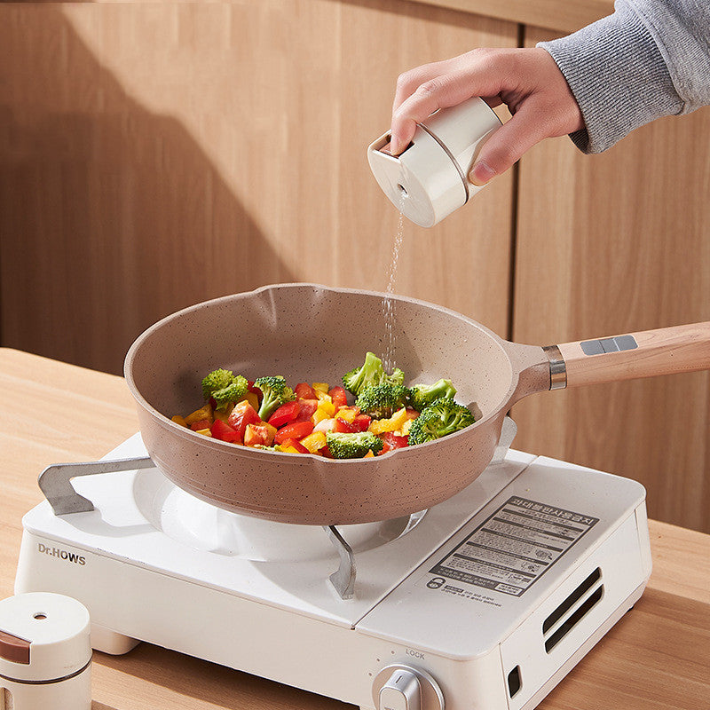 Hand sprinkling seasoning from a canister into a pan of stir-fried vegetables on a stovetop