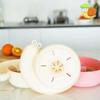 Cream snail-shaped basket on a kitchen counter next to oranges, with a pink basket of berries alongside