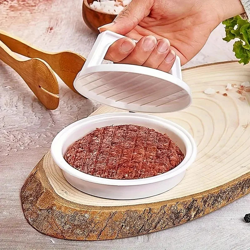 Hand pressing a raw beef patty in a white plastic burger press on a wood board with lettuce and wooden tongs