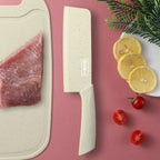 Cleaver-style knife next to raw meat on a cutting board with lemon slices and cherry tomatoes