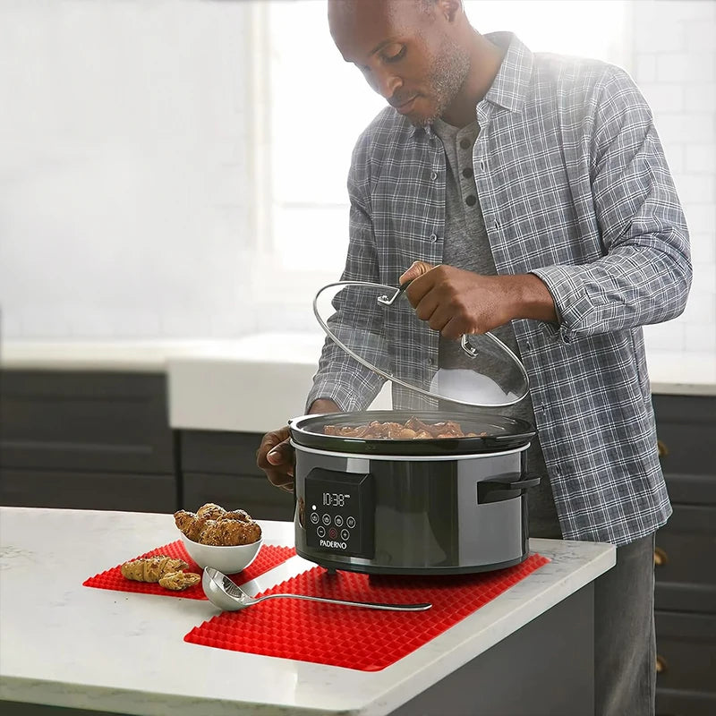 Red pyramid mat used as a trivet under a countertop slow cooker on a kitchen counter with croissants nearby