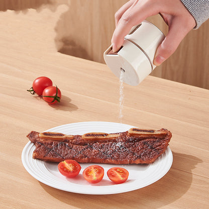 Hand shaking salt from a seasoning canister onto grilled ribs plated with cherry tomatoes